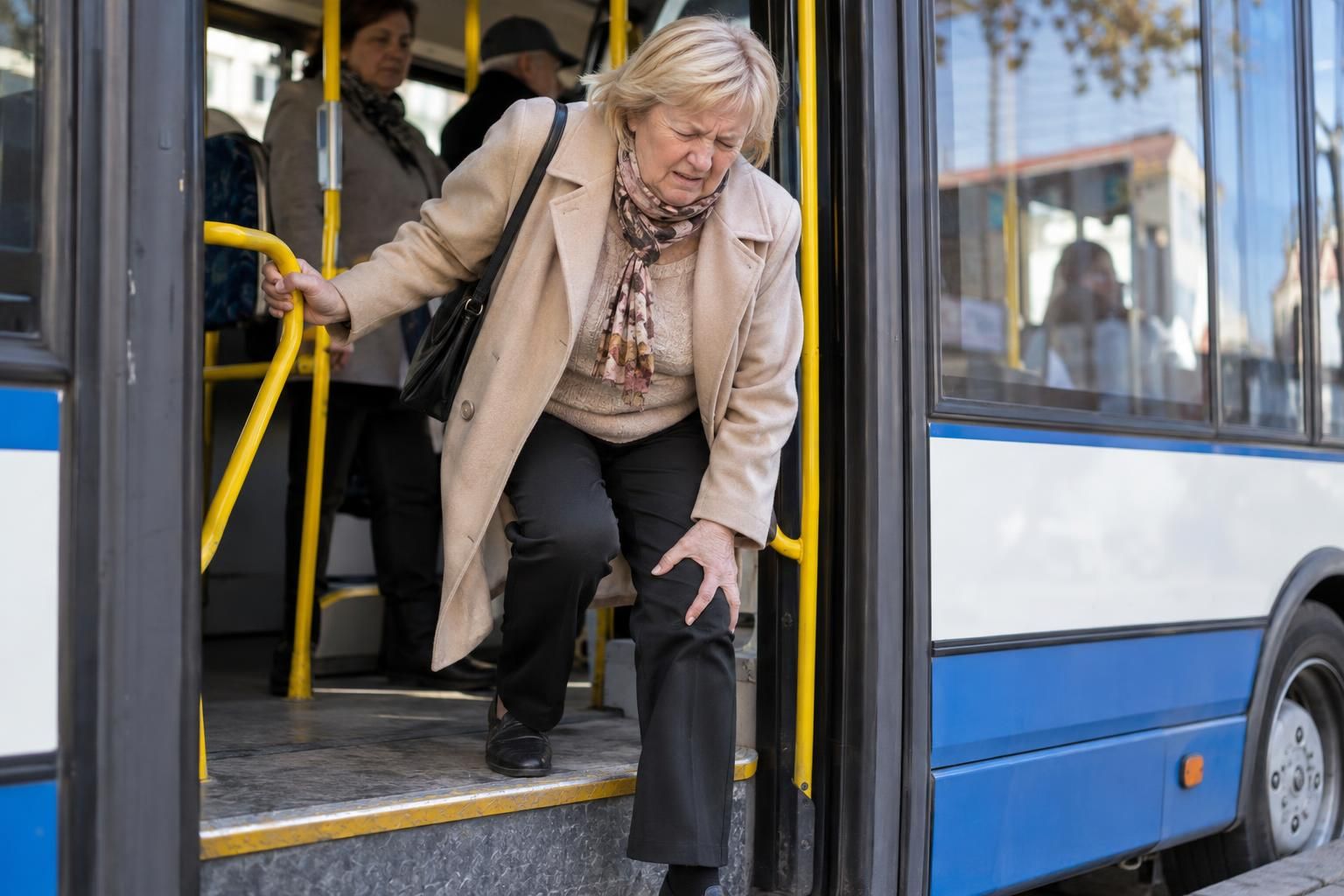 Ból kolan przy wysiadaniu z autobusu: kobieta trzyma się żółtej poręczy i łapie za kolano na ostatnim stopniu